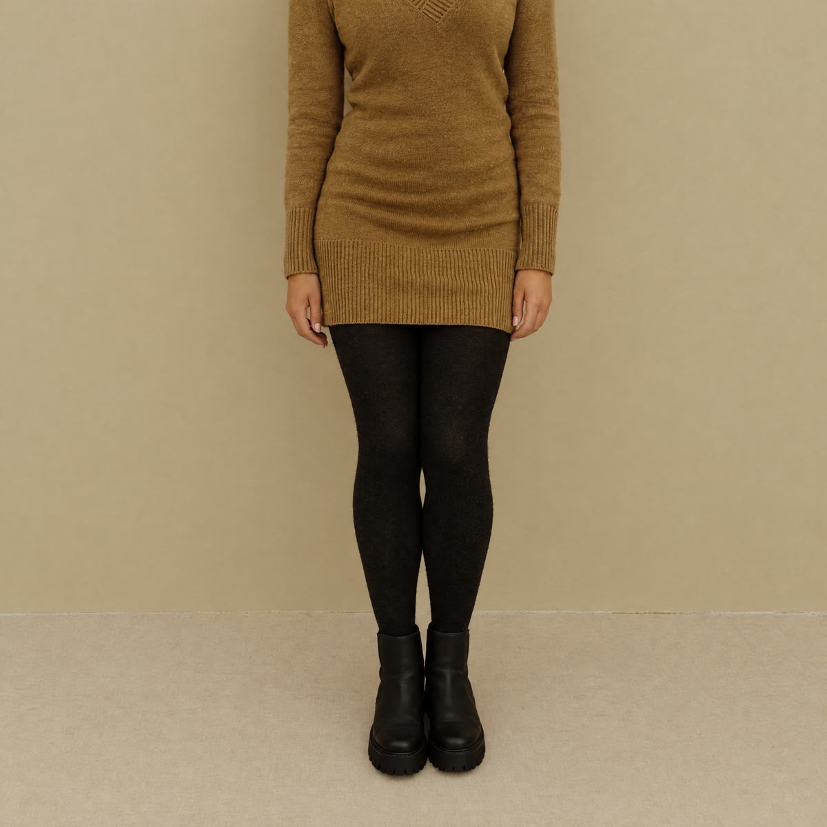 Jambes en collant noir épais et opaque, avec des bottines plates, sous une robe en maille camel.